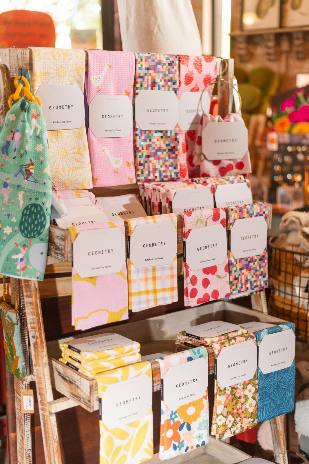 Display of folded patterned textiles with white labels on a wooden display stand.