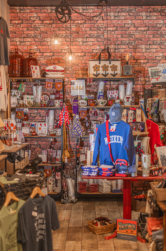 A retail shop with shelves displaying various merchandise against a brick wall. A red table features a blue sweater.