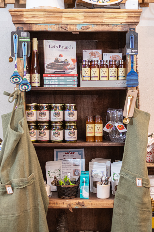 Wooden shelf with jars, bottles, cookbooks, and aprons; kitchenware display.