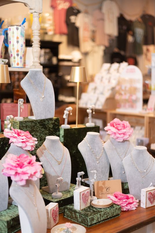 Jewelry display with necklaces on gray busts, accented by pink flowers and golden lighting.