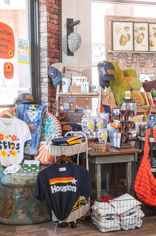Inside a Houston-themed gift shop, items include shirts, hats, a nest decor, and gifts, near a window.