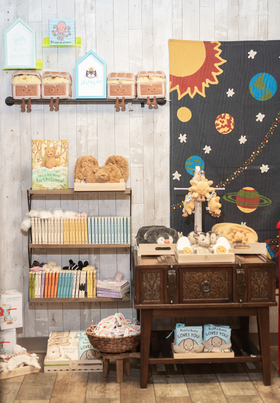 A children's store display featuring books, stuffed animals, and decorative houses on shelves.