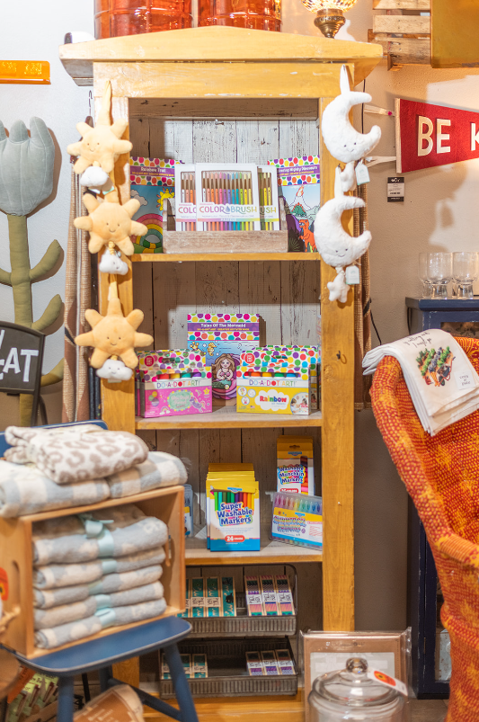 Wooden bookshelf filled with colorful products in a shop, sun and moon decorations hanging.
