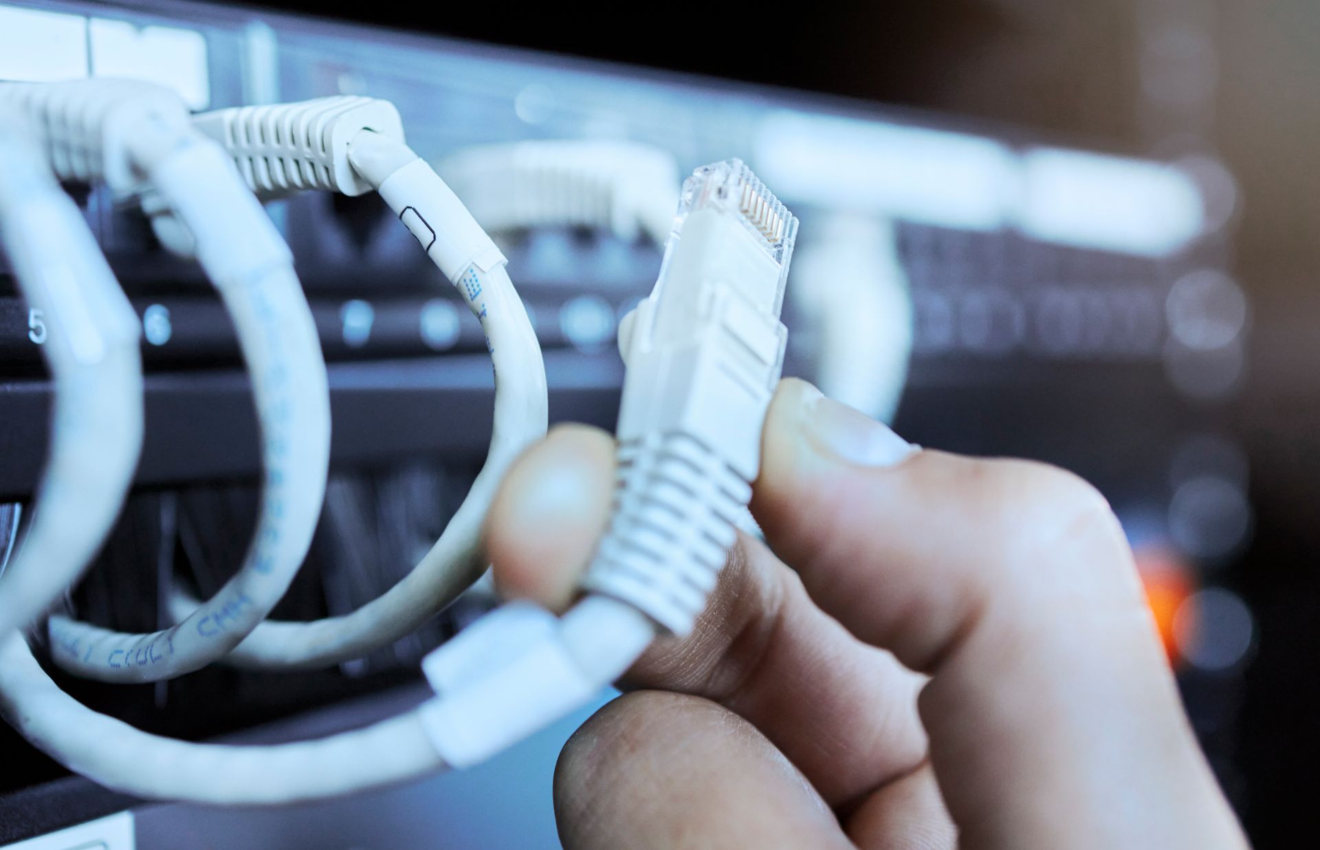 A person is holding a cable in their hand in front of a server.