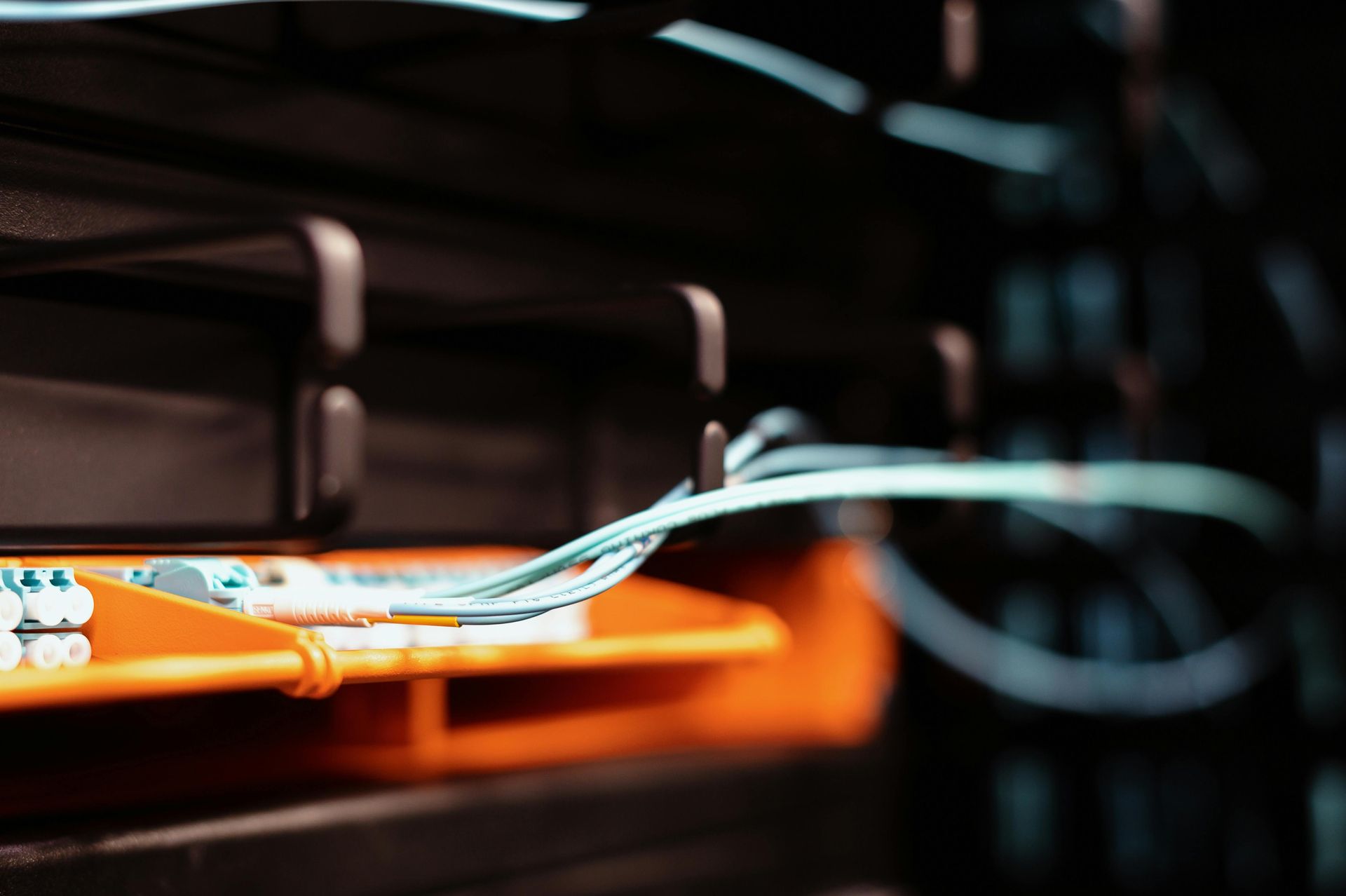 Close-up of server rack with network cables, orange panel and blue/white connectors, dark setting.