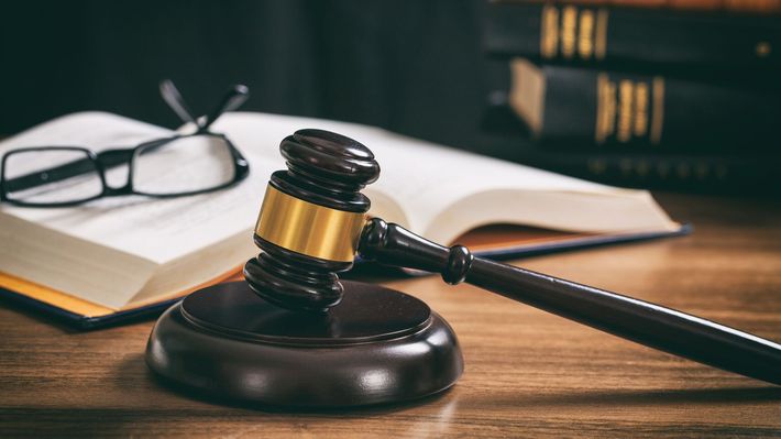 Judge gavel on wooden desk with law book and glasses, symbolizing justice and legal authority.