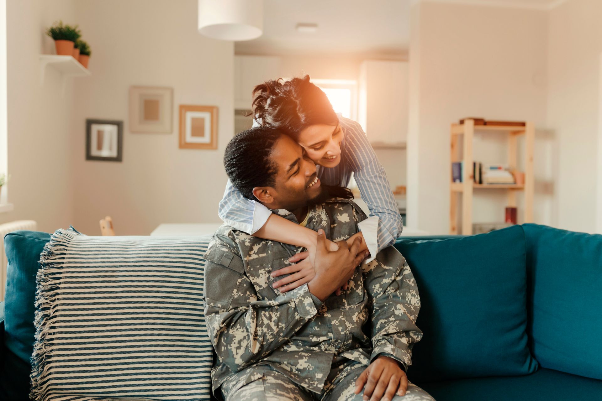 A woman is hugging a soldier who is sitting on a couch.