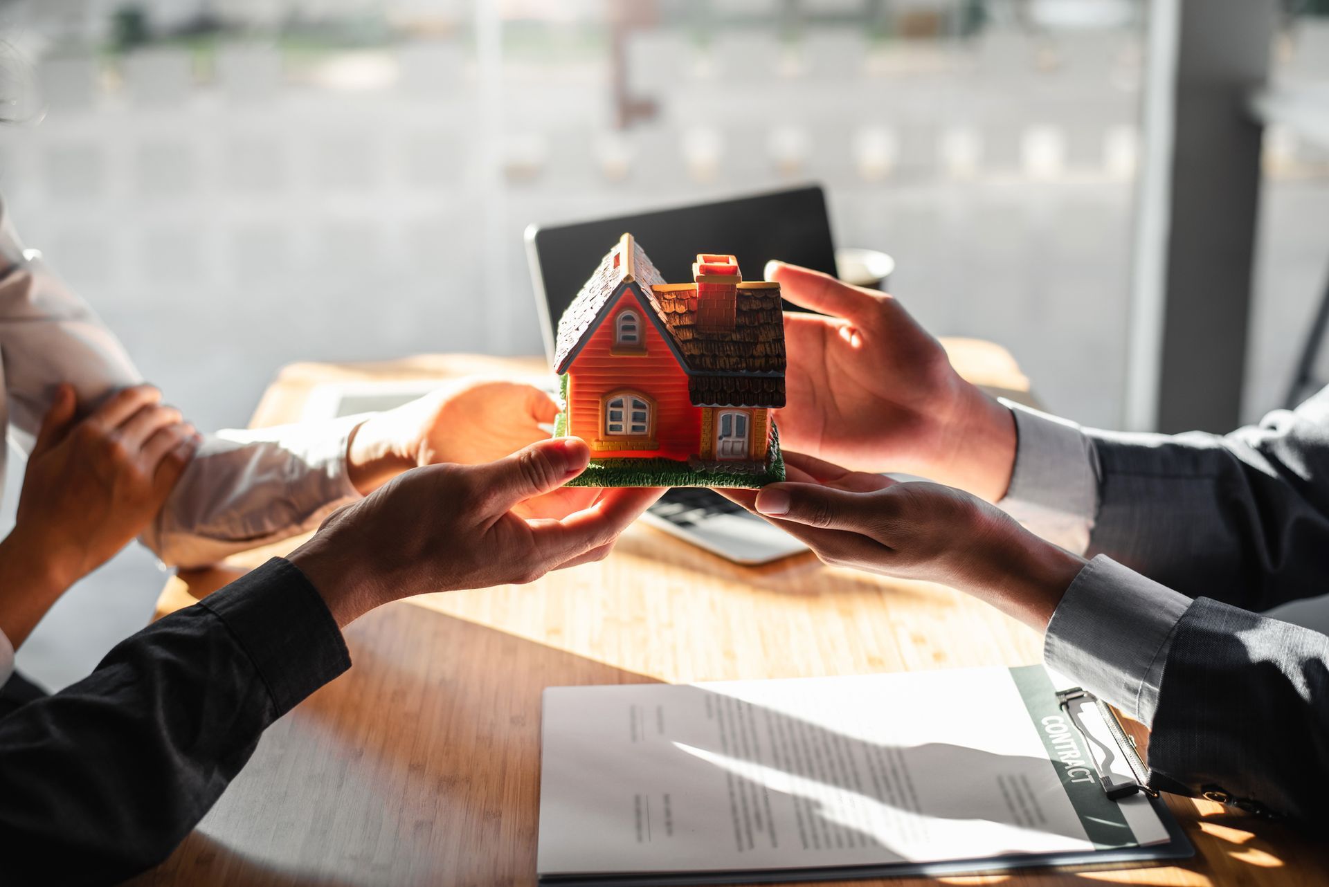 A man is holding a model house in his hands over a table.