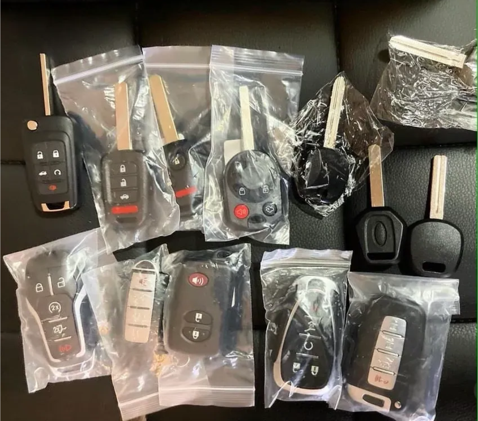 Keys in plastic bags, including car keys and fobs, arranged on a black surface.