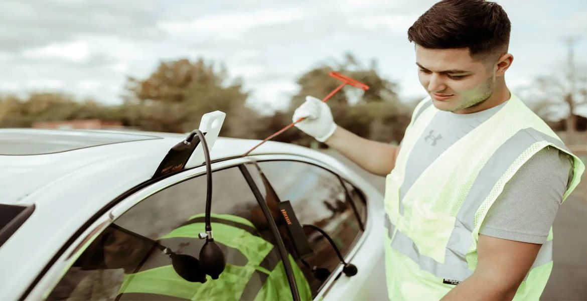 Person in a reflective vest unlocking a car door with a air wedge pump and tools