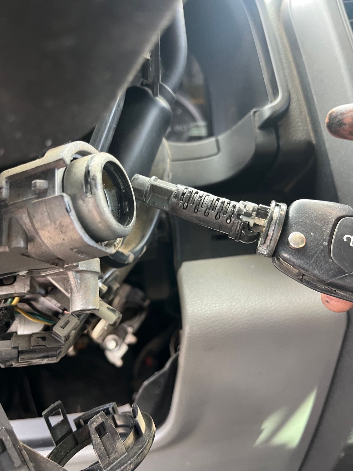 Broken steering column inside a car interior, with exposed wiring and metal components.
