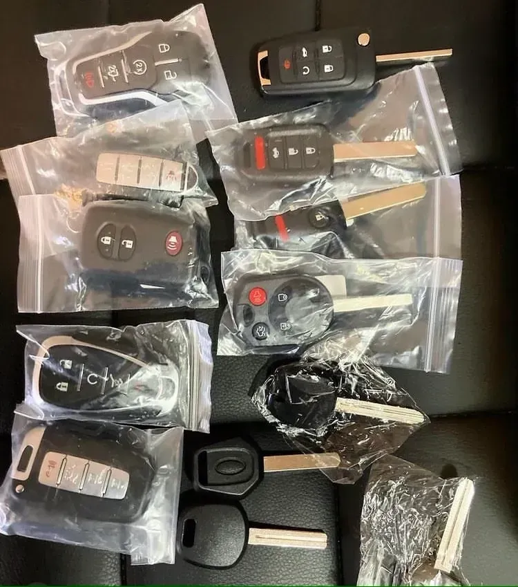 Keys in plastic bags, including car keys and fobs, arranged on a black surface.
