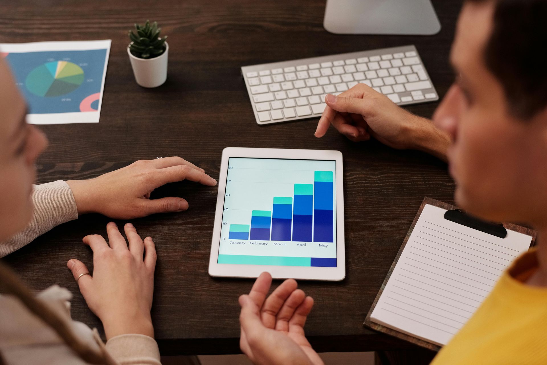 Team meeting around a tablet showing a blue bar chart on a wooden desk