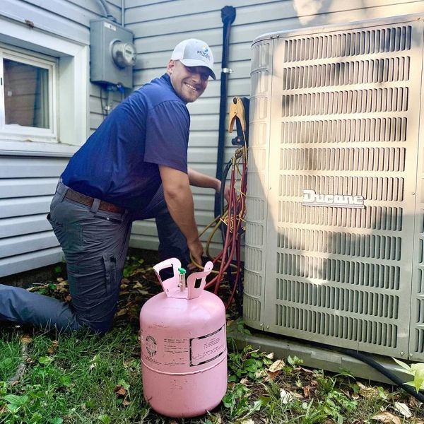 Moore Comfort HVAC technician working beside an outdoor Ducane air conditioning unit with refrigerant gauges and equipment.