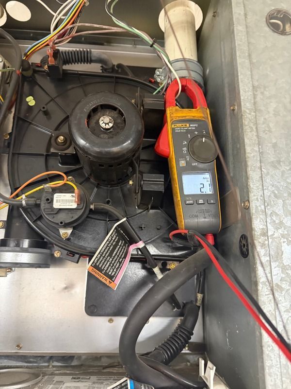 Digital clamp meter testing electrical current inside a residential furnace.