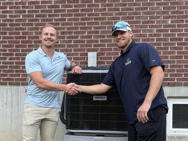 Moore Comfort HVAC technician shaking hands with a customer beside an outdoor air conditioning unit.