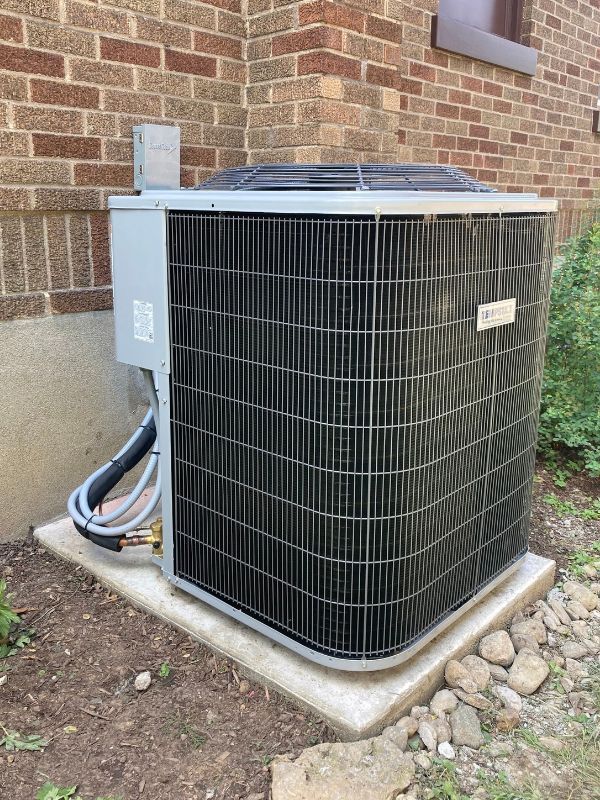 Residential Tempstar outdoor air conditioning condenser on a concrete pad beside a brick house.