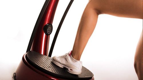 Person's foot in white sneaker on a red vibrating exercise machine.