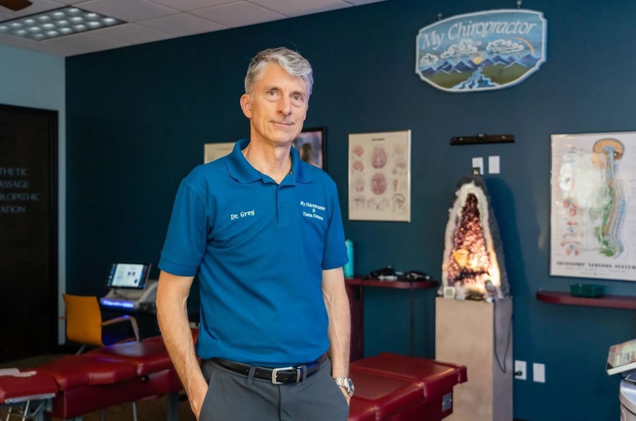 Man in blue shirt stands in chiropractic office, with medical equipment and posters.