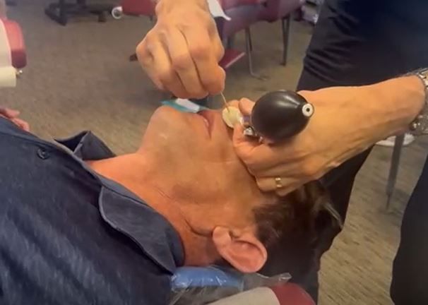 Man having a medical procedure on his eye. Hands using tools. Indoor setting with chairs.