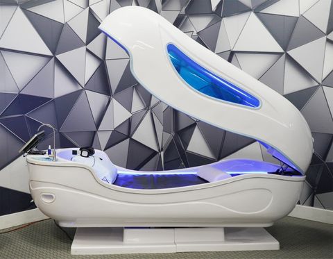 White spa bed with a blue light interior, against a geometric wall.