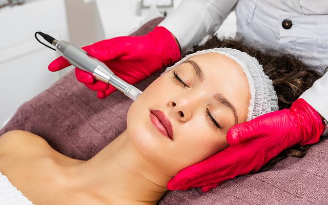 Woman receiving facial treatment. Technician with pink gloves holds device to face.