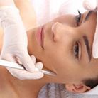 Woman undergoing facial treatment with gloved hands and a tool.