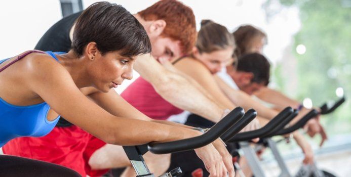 People of diverse backgrounds riding stationary bikes in a fitness class, indoors.