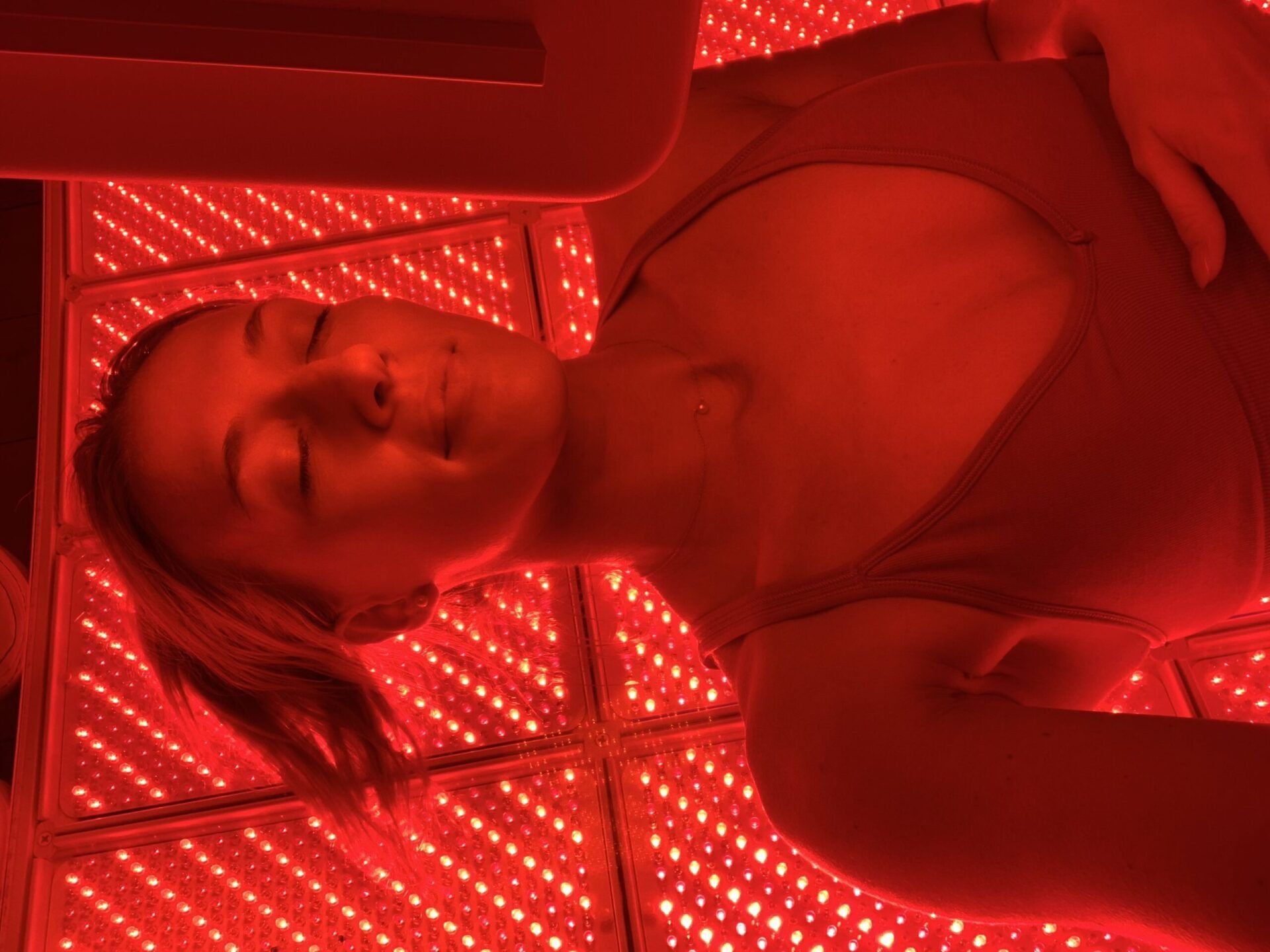 Woman receiving red light therapy, lying down with eyes closed.