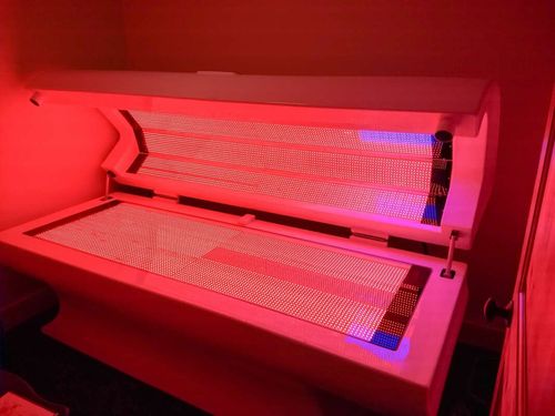 Red light therapy bed, open and illuminated, in a room.