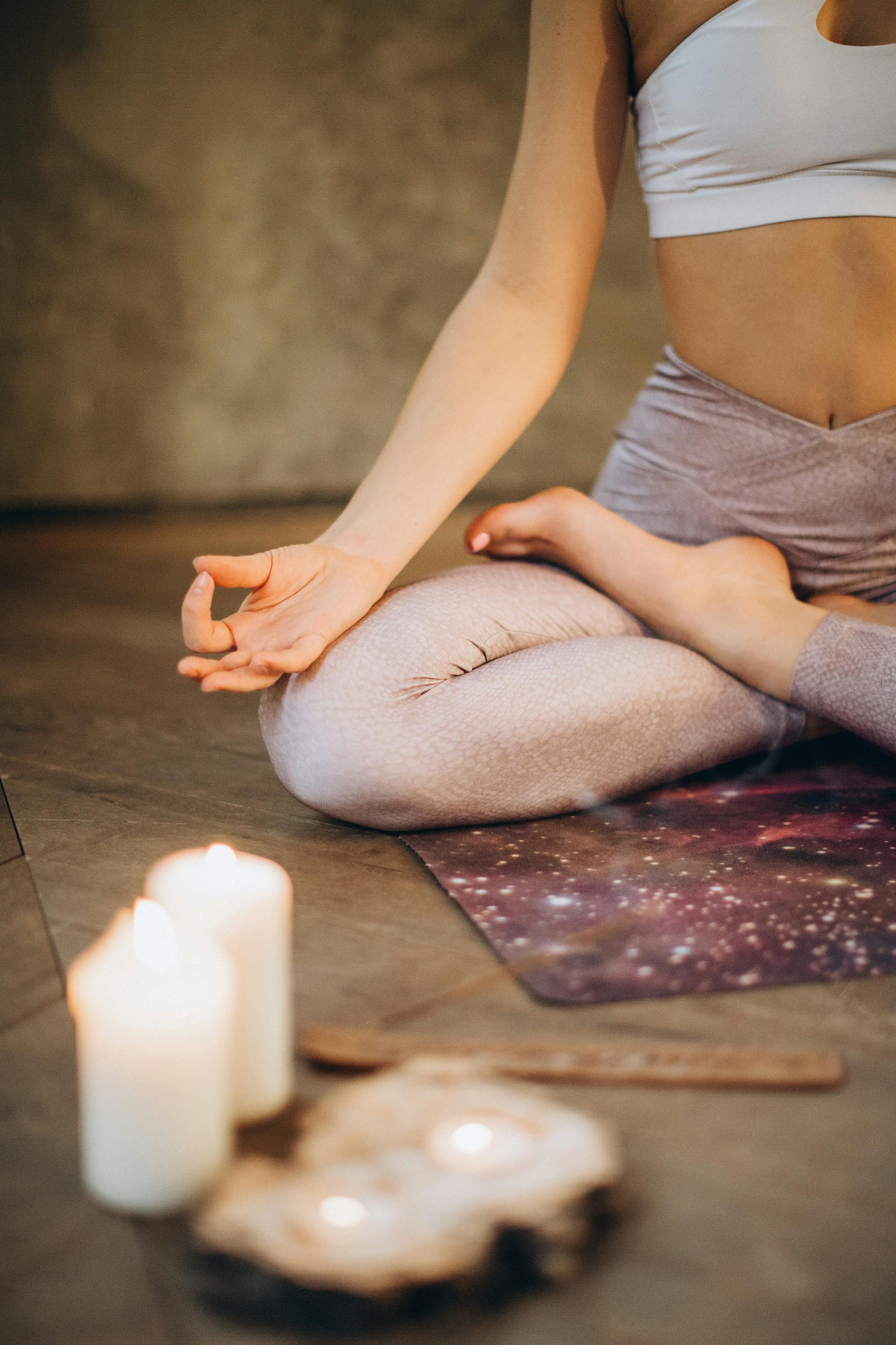 Woman in yoga pose with candles, setting on mat.