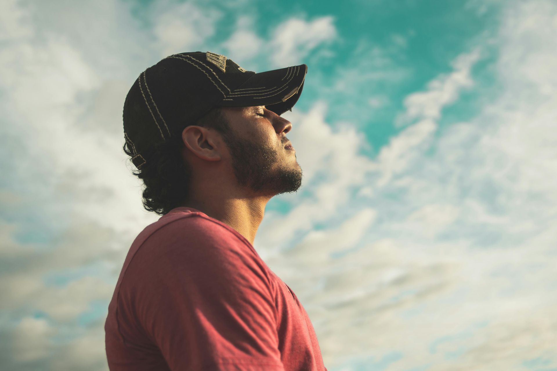 Man in cap looks up at the sky; side profile.