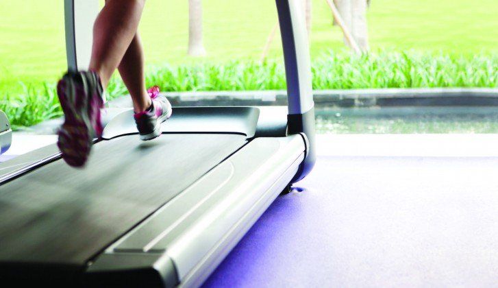 Person running on a treadmill with green grass and water visible through the window.