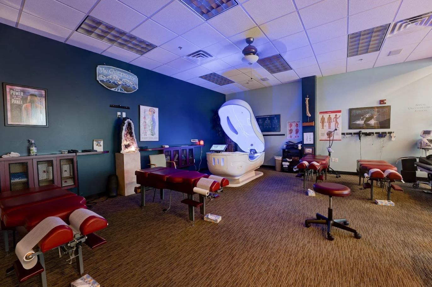 Chiropractic office: massage tables, therapy equipment, and a large white machine in a room with blue walls.