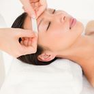 Woman getting eyebrow waxed at a spa. Eyes closed, hand holding wax strip to forehead.