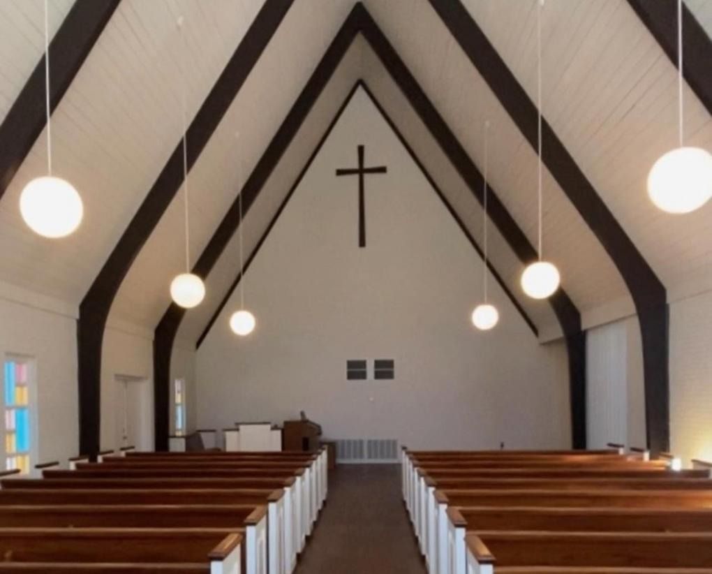Empty church interior with wooden pews, hanging lights, and a cross on the far wall