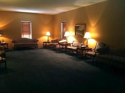 Dim living room with couch, chairs, lamps, and framed wall art