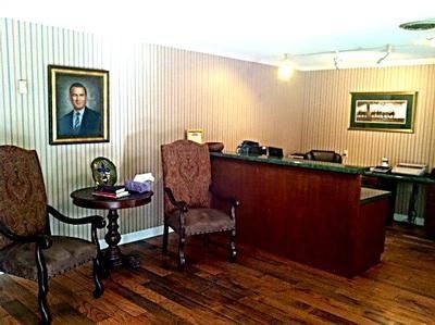 Small office with wood floors, desk, two chairs, framed portraits, and striped wallpaper.