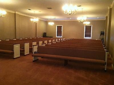 Empty church sanctuary with wooden pews, beige walls, chandeliers, and carpeted floor