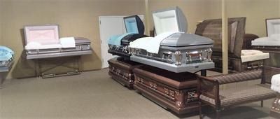 Two open caskets in a funeral home viewing room, with chairs and a small table nearby