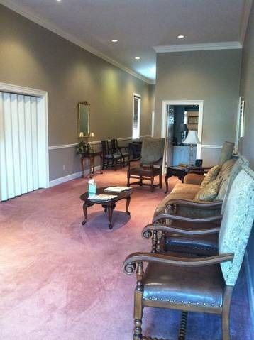 Empty waiting room with pink carpet, chairs along the wall, and a small table in the center