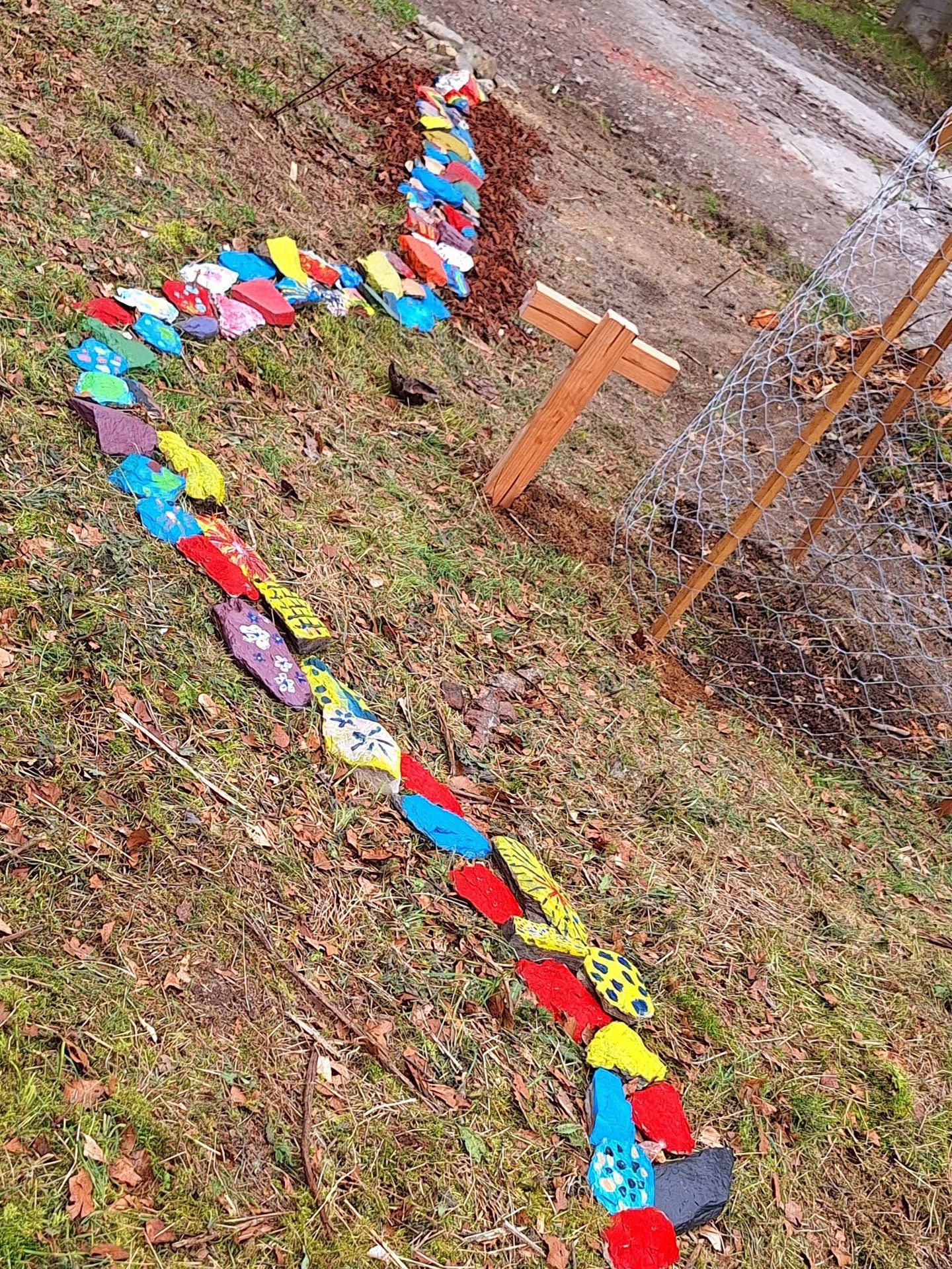 Eine bunte Schlange liegt im Gras neben einem Holzkreuz.