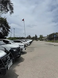 A line of white cars parked on a paved lot near a flag pole and buildings on a partly cloudy day.— Mt Isa Four Wheel Drive Services in Mount Isa City, QLD