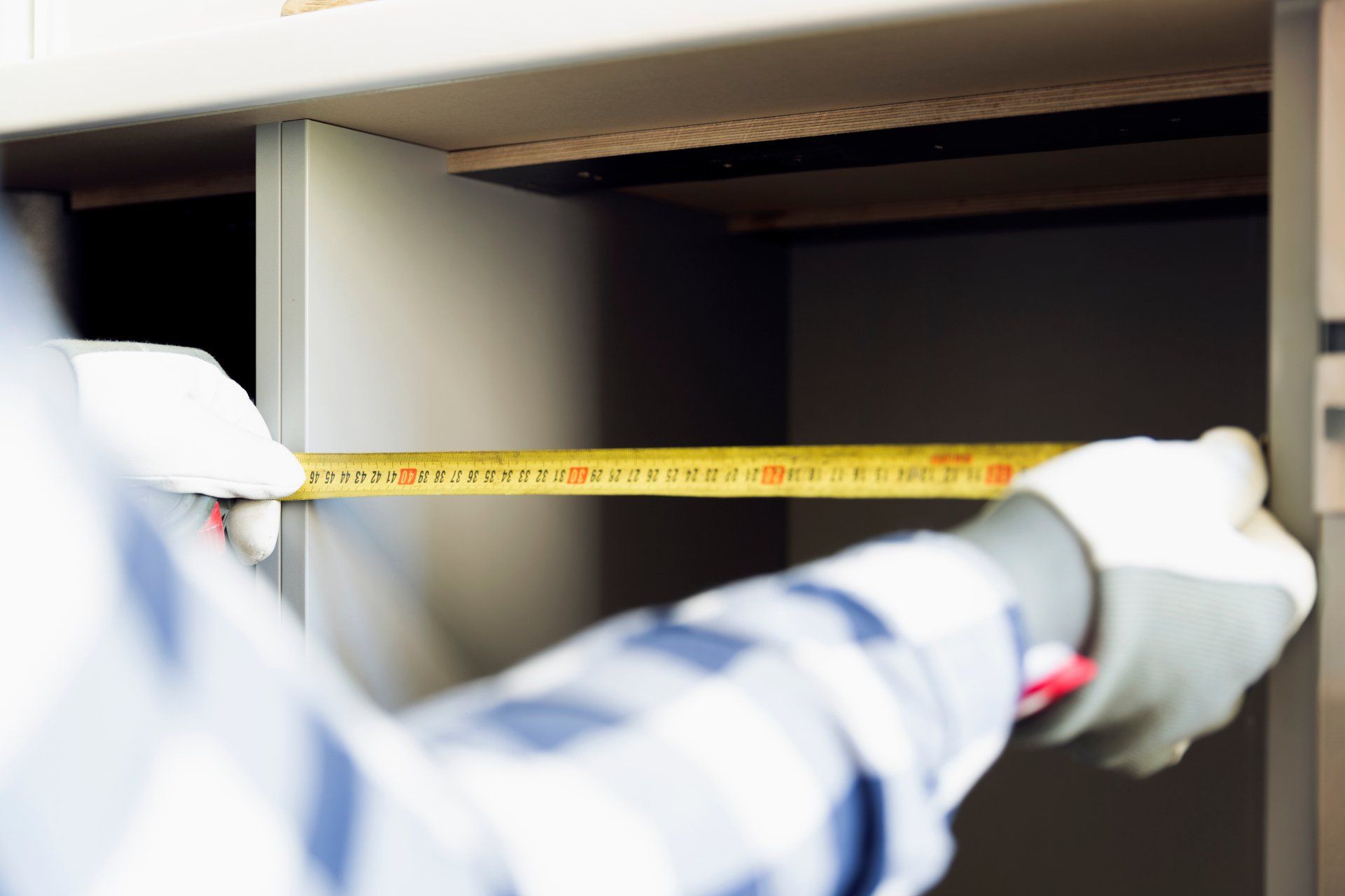 Une personne mesure une armoire avec un ruban à mesurer.