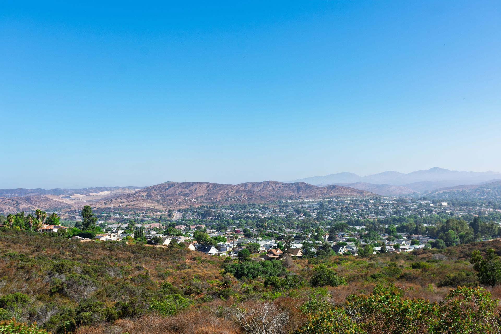 Wide cityscape with a hazy mountain backdrop under a clear blue sky Wide cityscape with a hazy mountain backdrop under a clear blue sky