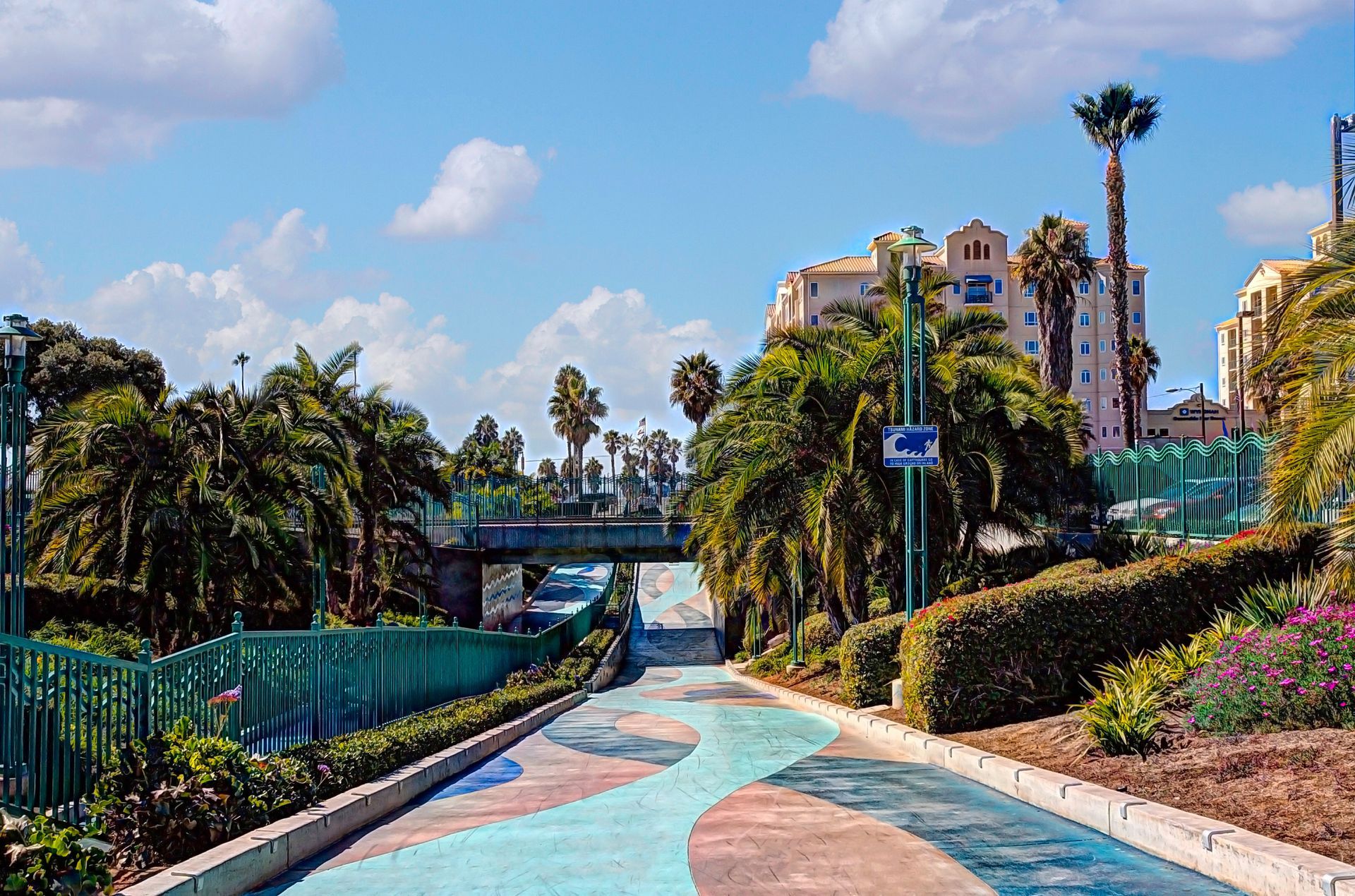 Curving colorful path through palm trees and flowers in a sunny tropical park with buildings in the background Curving colorful path through palm trees and flowers in a sunny tropical park with buildings in the background
