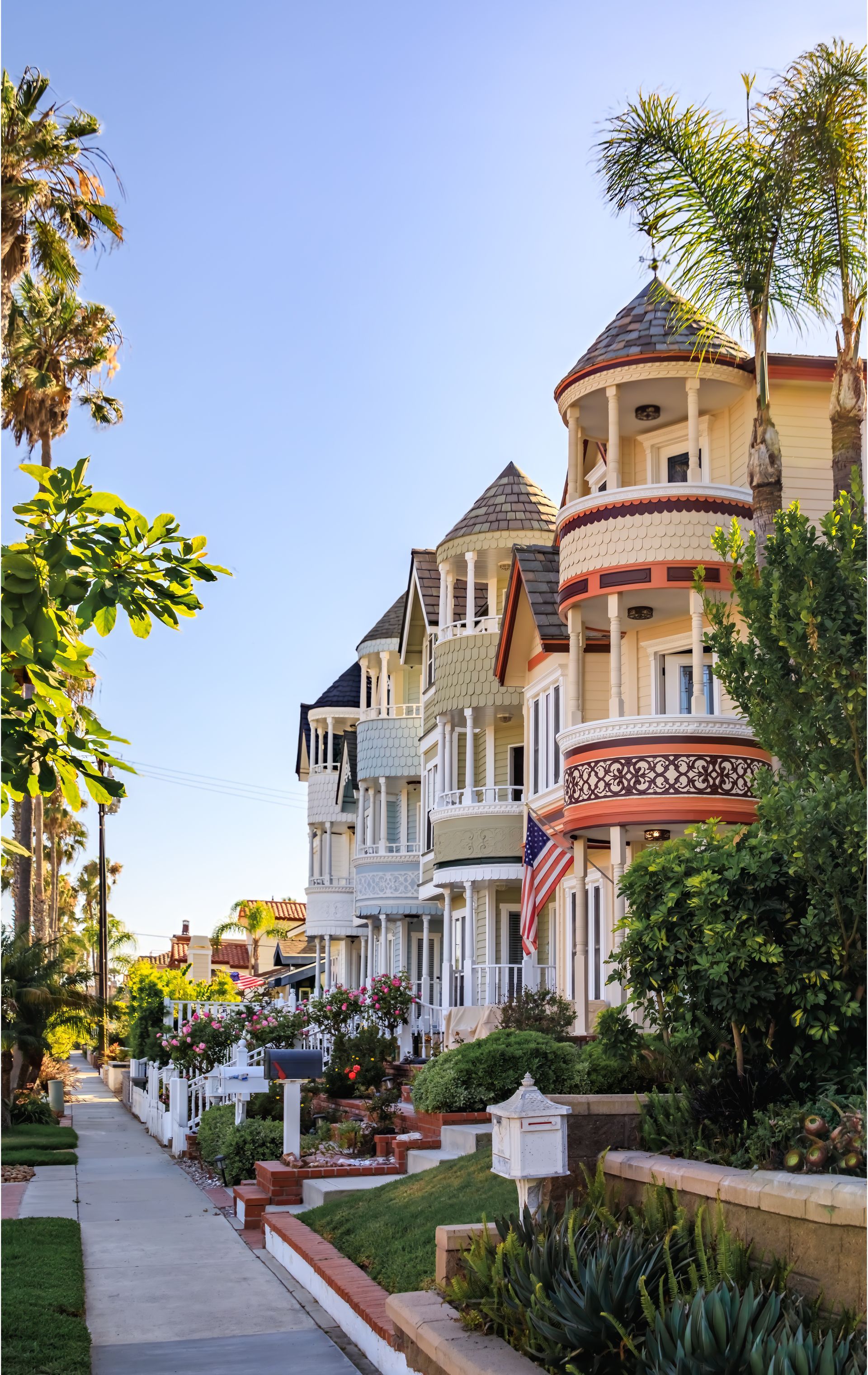 Tree-lined sidewalk beside ornate pastel Victorian houses on a sunny residential street Tree-lined sidewalk beside ornate pastel Victorian houses on a sunny residential street