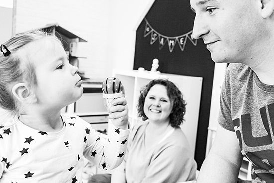 Een klein meisje drinkt uit een kopje terwijl een man en een vrouw toekijken.