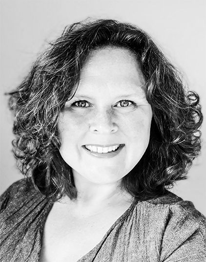 Een vrouw met krullend haar lacht op een zwart-witfoto.