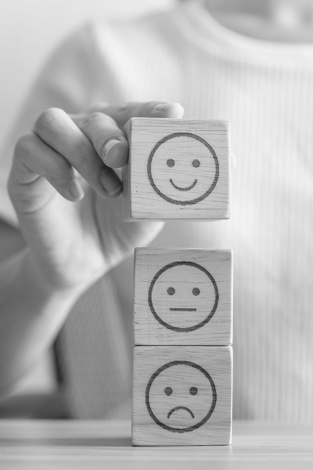 Een persoon houdt drie houten blokken vast met daarop getekende smileys.
